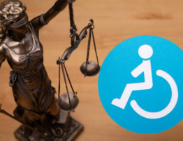 A blue, circular handicap wheelchair sign being held up next to a bronze lady of justice statue.
