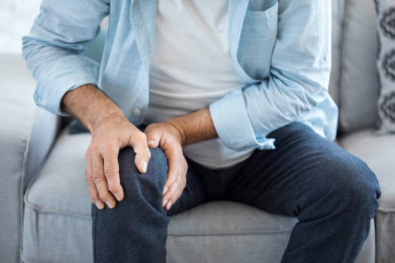 A man sitting on a couch holding his knee due to arthritis pain.