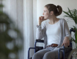 Woman in a wheelchair staring pensively out a window.